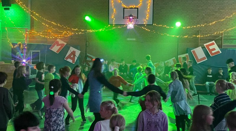Zur Belohnung ab zur Party Bereits zum vierten Mal in Folge organisierte die Schulpflegschaft der Marienschule Hauenhorst am Tag der Ausgabe der Halbjahreszeugnisse zur Freude aller die beliebte „Zeugnisdisco“. Ob Erst- oder Viertklässler, Dancing-Queen oder eher Tanzmuffel, ob gutes oder weniger gutes Zeugnis – alle waren da. Und natürlich hat sich auch in diesem Jahr das Kommen mal wieder mehr als gelohnt. Die vom erfolgreichen Crowdfunding angeschaffte Soundanlage und die tanzwütigen Kids brachten die Halle zum Beben. DJ Sven spielte was die Kinder sich wünschten. Discolichter wohin man schaute, eine gut funktionierende Nebelmaschine und der Lieblingsflashmob der Marienschülerinnen und Marienschüler unter der Leitung der momentan abgeordneten Kollegin Maike Hüls sorgten für allerbeste Stimmung. Zwischendurch konnten sich alle an ihren vorbereiteten Tischen mit Getränken und Snacks stärken. Für die Ausgabe der Hotdogs ging man Jahrgangsweise zum discomäßig verkleideten Team der Schulpflegschaft. Auch hier sorgte eine perfekte Organisation für einen reibungslosen Ablauf. Zwei Stunden waren schnell vorbei, nachwirken wird die Disco jedoch auf jeden Fall noch lange. Und: Erfolg verpflichtet. Ganz bestimmt dürfen sich die Kids in Hauenhorst auch im Schuljahr 2026/27 am Tag der Halbjahreszeugnisse auf die fünfte Auflage der „Marienschulzeugnisdisco 2027“ freuen.
