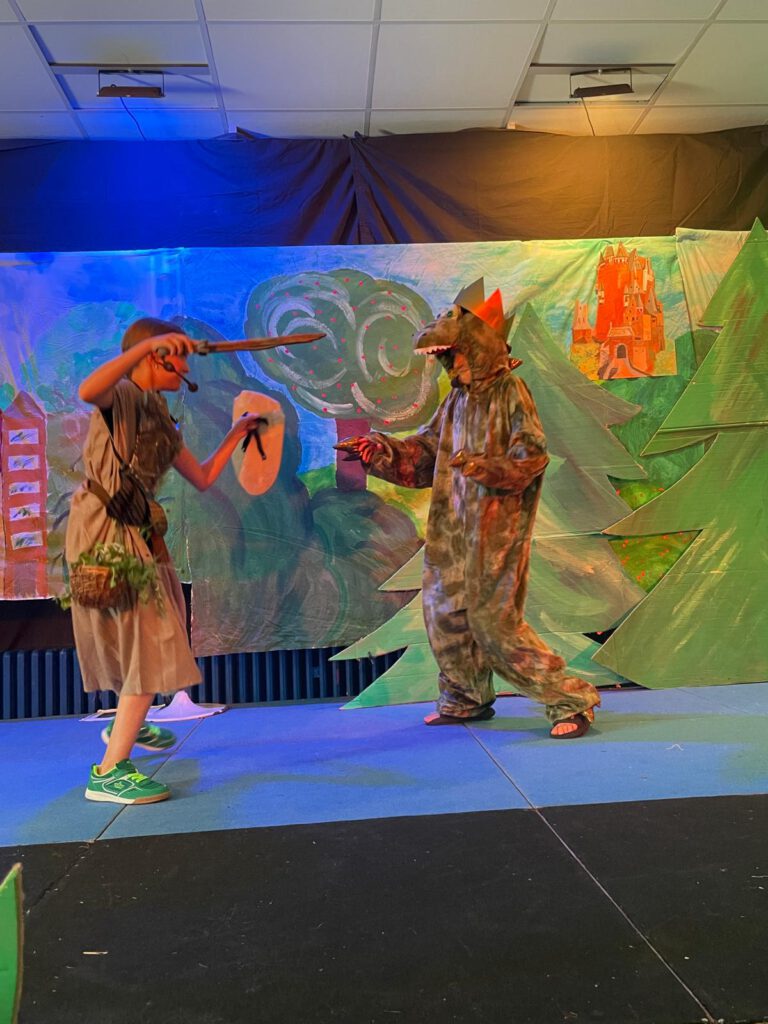 „Den Fluch besiegt“ – Hauenhorster Kinder führen Musical auf
Und wieder einmal stand das aktive Schulleben der Marienschule aus Hauenhorst ganz im Zeichen des NRW- Landesprogramms „Kultur und Schule“, mit dessen finanzieller Unterstützung der Schulchor der Hauenhorster Grundschule im laufenden Schuljahr ein großartiges Musical auf die Bühne bringen konnte. 
Aufgeführt wurde in diesem Jahr das Musical „Drachenkämpfer - vom Bauernjungen zum Königssohn“ von Uli Führe und Babette Dieterich.
Drei Mal wurde das Stück am vergangenen Freitag bei über 30 Grad Außentemperatur und bestimmt 40 Grad Innentemperatur in der stets voll besetzten Aula der Schule aufgeführt. Traditionell sind zur Generalprobe die kommenden Schulneulinge aus den Hauenhorster Kindergärten eingeladen und schauen sich gemeinsam mit den anderen Marienschülerinnen und -schülern die Generalprobe des jeweiligen Musicals an. Am Nachmittag durften/mussten die jungen Künstler dann noch zwei Mal vor den stolzen Augen der Eltern, Großeltern und Freunden ihre gesanglichen, instrumentellen, tänzerischen und schauspielerischen Fähigkeiten unter Beweis stellen.
Die Zuschauer erlebten ein spannendes Musical, in dem es um einen furchterregenden Drachen geht, der Jahr für Jahr ein Mädchen des Königreiches fordert, um seine Wut zu besänftigen. Die Dorfbewohner leben in ständiger Angst, dass ihre Tochter ausgewählt und zum Drachen geschickt wird. Keinem Ritter ist es bisher gelungen, den Drachen zu besiegen. Der junge Burkhardt nimmt den Kampf mutig auf und erlöst den Drachen mit geheimnisvollen Kräutern und einer verzauberten Rüstung von seinem bösen Fluch. Am Ende bekommt der mutige Burkhardt als Dank die schöne Königstochter zur Frau.
In bezaubernden Kostümen und verschiedensten Rollen zeigten die ca. 60 Mädchen und Jungen ihre schauspielerische und gesangliche Freude und Kompetenz. Zum Schluss aller drei Aufführungen gab es für alle Akteure einen riesigen Applaus und begeisterte Worte vom Schulleiter Christian Hülsmann. Seine warmen Worte (bei 40 Grad kann man das durchaus so bezeichnen) richteten sich gleichermaßen an die Kids als auch an die Künstlerin Brigitte Lesting und die Lehrkraft Sabine Müller für die beeindruckende Inszenierung dieses wunderschönen Stückes. 
Im Anschluss feierte die Schulgemeinschaft dann noch das ebenfalls traditionelle „Come together“ auf dem Schulhof und ließ den erfolgreichen und zum Glück trockenen Tag in gemütlicher Runde mit Popcorn, Zuckerwatte, Snacks, Grillwürsten im Brötchen und kalten Getränken ausklingen.  